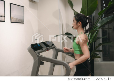 一名身穿訓練服的年輕女子在健身房的跑步機上跑步 一名身穿訓練服的年輕女子在健身房的跑步機上跑步 122928212