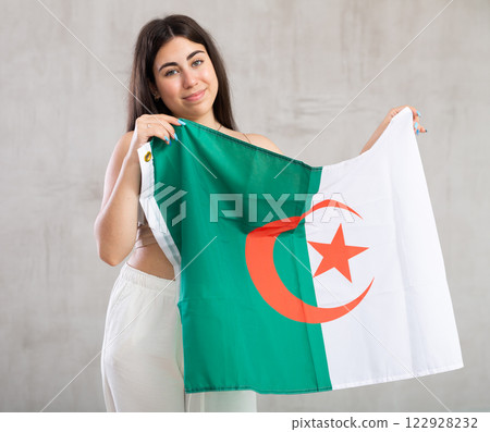 Happy young woman with flag of Algeria against unicoloured background 122928232