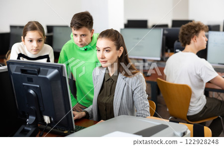 Female teacher and teenager pupils looking at monitor of PC 122928248