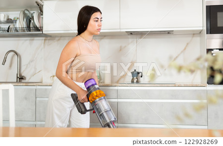Positive young woman vacuum-cleaning the floor in the kitchen 122928269