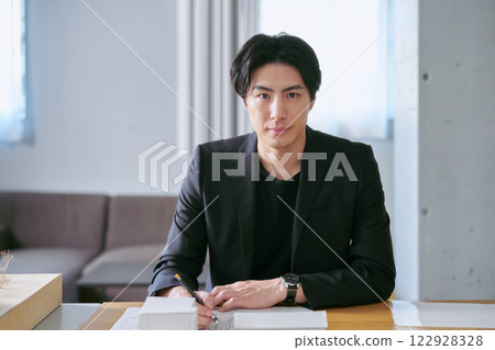 一位男建築師在設計建築時看著鏡頭，在建築模型前繪製藍圖 122928328