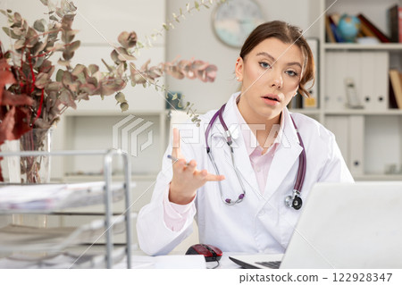 Positive woman doctor sitting at workplace with computer in office 122928347