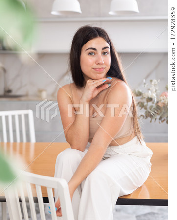 Smiling young woman posing sitting on kitchen table 122928359