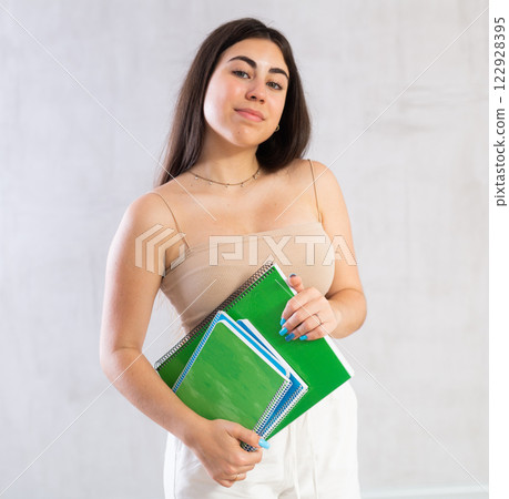 Young woman posing with notebooks against wall Young woman posing with notebooks against wall 122928395
