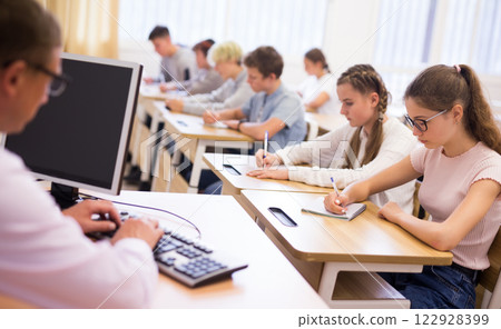 Teenagers listening to lecturer and writing in notebooks in classroom Teenagers listening to lecturer and writing in notebooks in classroom 122928399