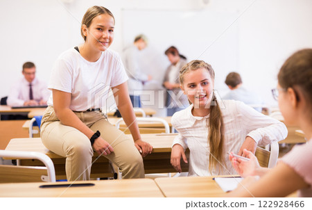 Teenage girls classmates communicating in classroom during break 122928466