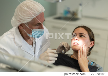 Mature man doctor dentist in white coat examines oral cavity of girl patient in dentistry. 122928483