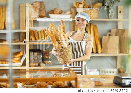 Bakery young woman employee holds basket of ready-made baguettes 122928502