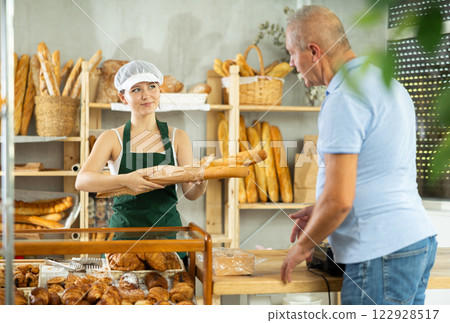 Female saleswoman hands hot baguettes to an elderly customer in bakery interior 122928517