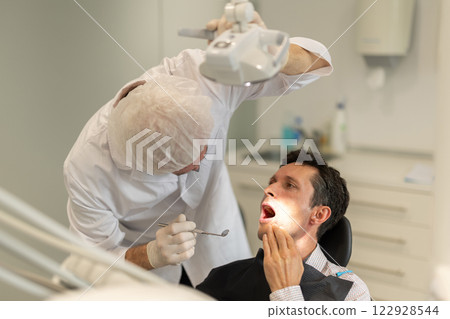 Elderly male dentist examining male patient 122928544