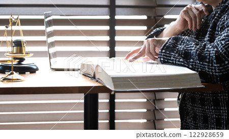 Legal professional reading law book at desk with justice scale, gavel, and laptop, legal research, judgment, and professional decision-making in law practice Legal professional reading law book at desk with justice scale, gavel, and laptop, legal research, judgment, and professional decision-making in law practice 122928659