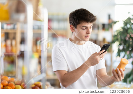 In shop young man scans QR code and take reading on sauce package using phone camera 122928696