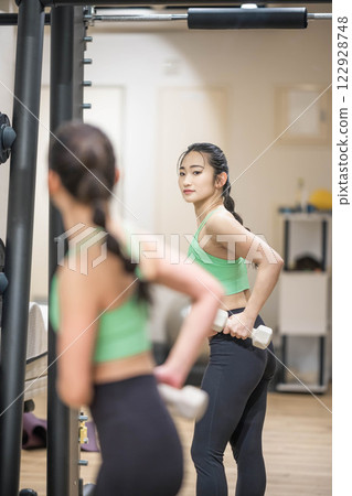 A young woman wearing training clothes doing muscle training with dumbbells 122928748