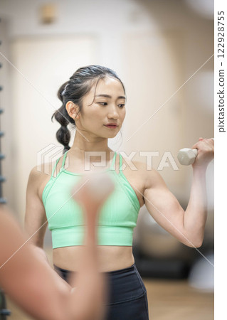 A young woman wearing training clothes doing muscle training with dumbbells 122928755