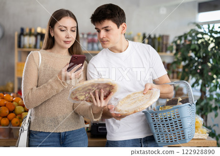 Positive young satisfied family couple choosing chilled pizza in market and scan QR code Positive young satisfied family couple choosing chilled pizza in market and scan QR code 122928890