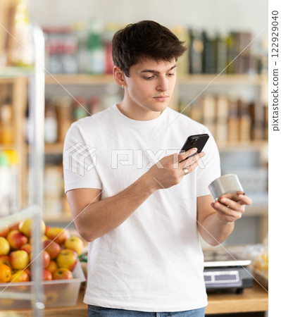 Guy scanning barcode on canned food while shopping in grocery store Guy scanning barcode on canned food while shopping in grocery store 122929040