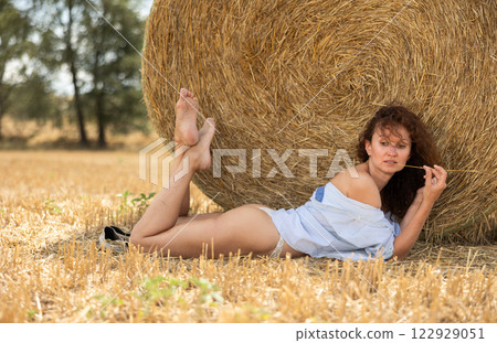 Half-naked girl in white light linen shirt poses lying in nature in field 122929051