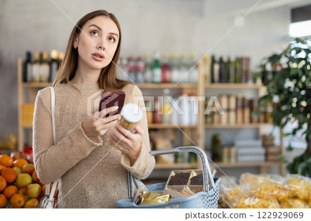 Female shopper scanning barcode on jar of pickled asparagus in supermarket 122929069