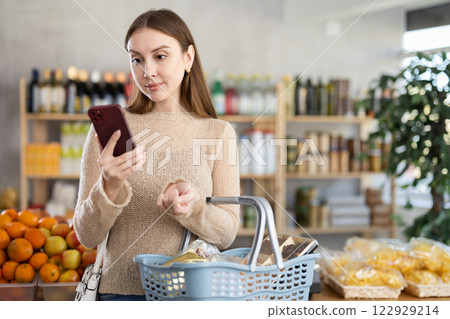 Visiting store, girl scrolling phone screen and looking for something in showcase. 122929214