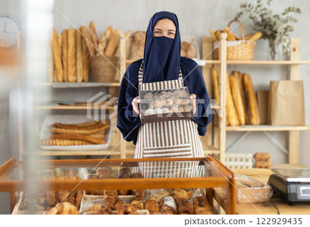European Muslim woman bakery worker sells cookies in box, stand at counter and wait for visitors European Muslim woman bakery worker sells cookies in box, stand at counter and wait for visitors 122929435