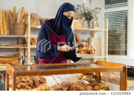 Middle-aged Muslim saleswoman puts croissants in display-case 122929464