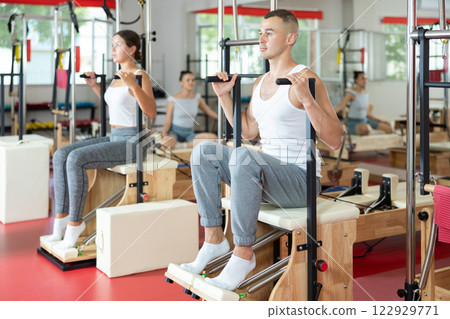 Young man doing arm exercises on pilates machine Young man doing arm exercises on pilates machine 122929771