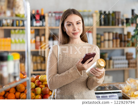 Young woman customer at shop scans QR code on beer can package using phone camera 122929794