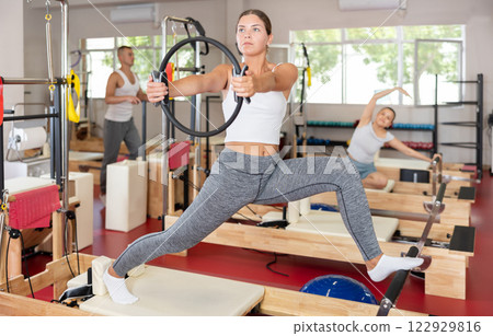 Sportive young girl training her arms and legs on reformer device 122929816