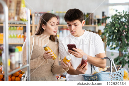 Young girl with husband in supermarket scan QR code bottle of smoothie. Couple of buyers friends take photo information on packaging of bio product 122929884