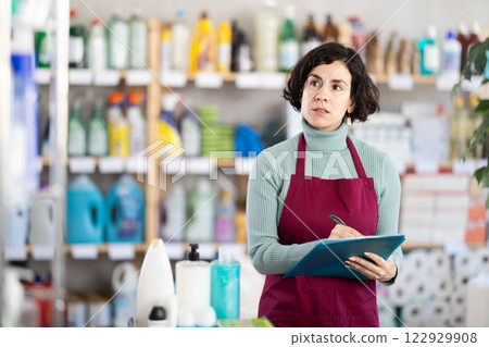 Middle-aged woman taking record of inventory in household store Middle-aged woman taking record of inventory in household store 122929908