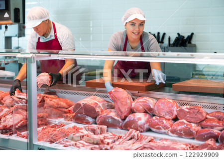 Young butcher shop saleswoman laying out raw beef in display case 122929909