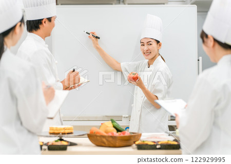 A female instructor teaching at a chef seminar, vocational school, and employee training, and male and female students (in the food service industry) A female instructor teaching at a chef seminar, vocational school, and employee training, and male and female students (in the food service industry) 122929995