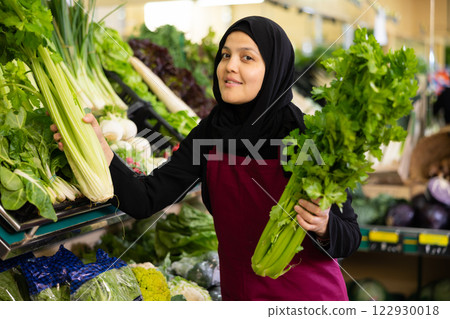 Muslim female seller in apron takes celery leaf from window 122930018