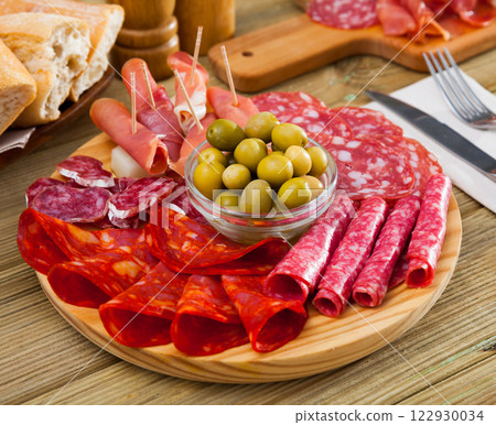 Cold cuts from ham, sausages on wooden plate Cold cuts from ham, sausages on wooden plate 122930034