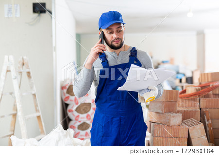 Builder with documents is talking on a mobile phone 122930184