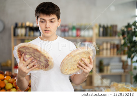 Male buyer carefully reads labels on frozen pizza - she chooses the best product in supermarket 122930218