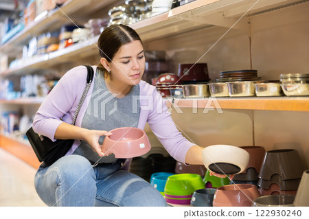 Young woman choosing food and water bowls in pet shop 122930240