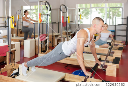 Young man training his abs on pilates reformer Young man training his abs on pilates reformer 122930262