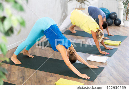 Middle-aged woman practicing downward facing dog pose of yoga in fitness room 122930369