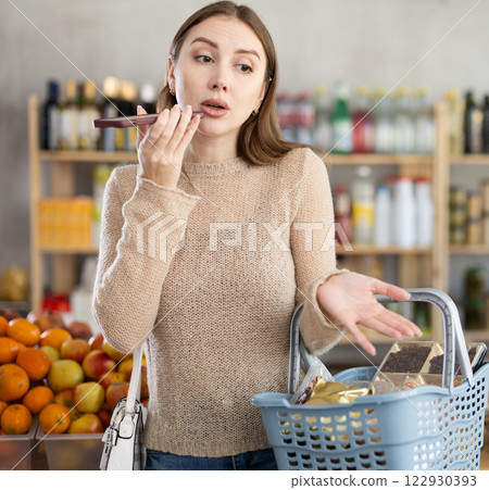 Woman chatting on speakerphone of smartphone while shopping in grocery store Woman chatting on speakerphone of smartphone while shopping in grocery store 122930393