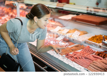 Young woman buyer chooses sausages in butcher shop Young woman buyer chooses sausages in butcher shop 122930413