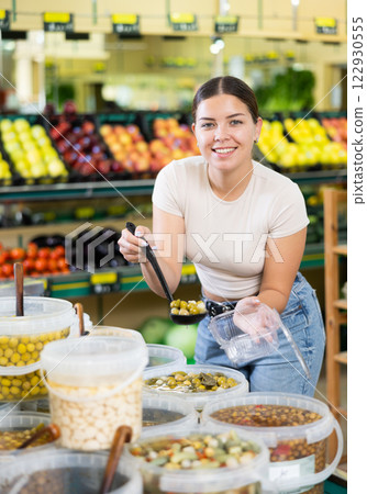 Young woman puts handful of olives in disposable container with ladle 122930555