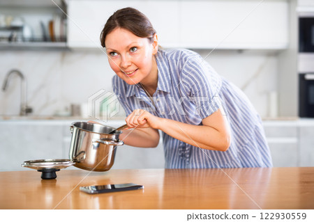 Inexperienced housewife holds saucepan in hands and calls asking for cooking advice 122930559