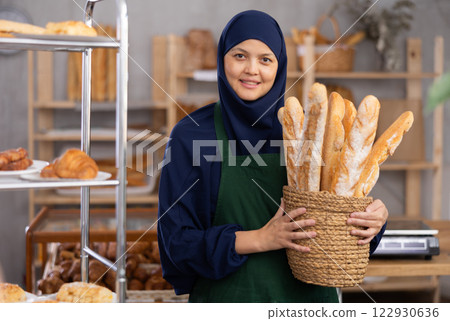 Middle-aged Muslim saleswoman displays baguettes in wicker basket 122930636