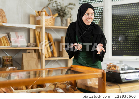 Saleswoman in a hijab collects pastries in a container 122930666