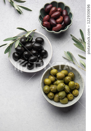 Black, green and kalamata olives with olive branches on marble background Black, green and kalamata olives with olive branches on marble background 122930696