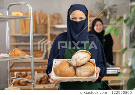 Positive woman seller of oriental bakery in niqab with fresh hot pastries in hands Positive woman seller of oriental bakery in niqab with fresh hot pastries in hands 122930860