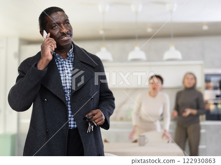 Middle-aged man ready to leave talking on phone while two women scolding him behind 122930863