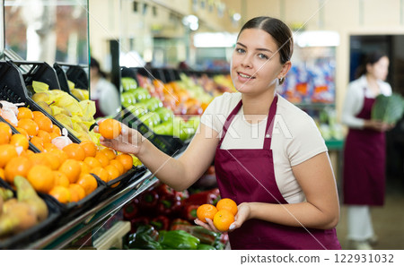 Young woman wearing apron working with fresh tangerines on supermarket Young woman wearing apron working with fresh tangerines on supermarket 122931032