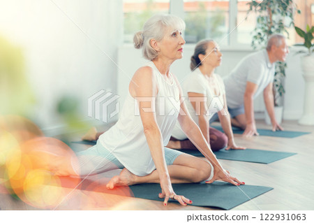 Elderly women together with a young coach doing stretching and doing yoga on mats in gym 122931063